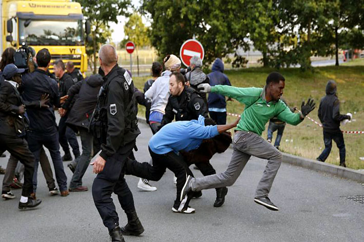 À Calais, des policiers empêchent des migrants de s'accrocher aux camions qui se dirigent au Royaume-Uni - © Le Figaro