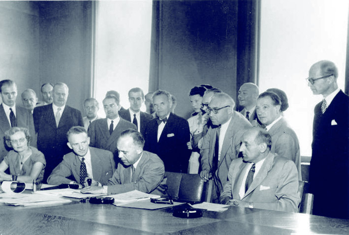 Signature de la Convention de Genève de 1951. Les trois hommes assis (g-d): M. John Humphrey, Directeur du Dép. des Droits de l'Homme; M. Knud Larsen (Danemark) Président de la Conférence; Dr. G.V. van Heuven Gödhart, Haut Commisssaire pour les Réfugés. - © Arni / UN Archives / August 1, 1951